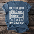 Blue t-shirt with "God forbid women have hobbies" and witchy items graphic.