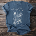 Blue t-shirt with white line art of a witch profile surrounded by Jimsonweed and Deadly Nightshade plants.
