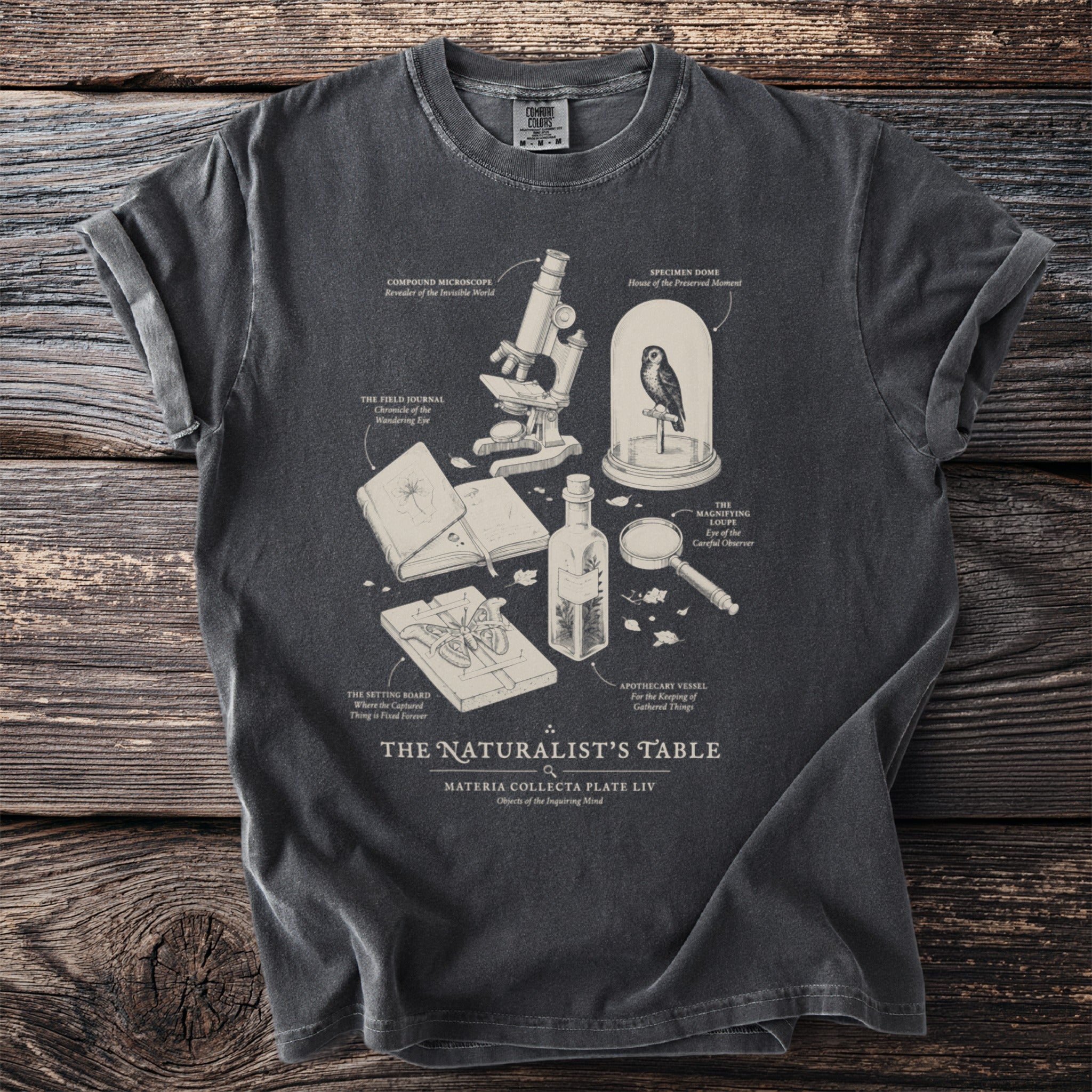 Dark grey t-shirt with a naturalist's table illustration and text.