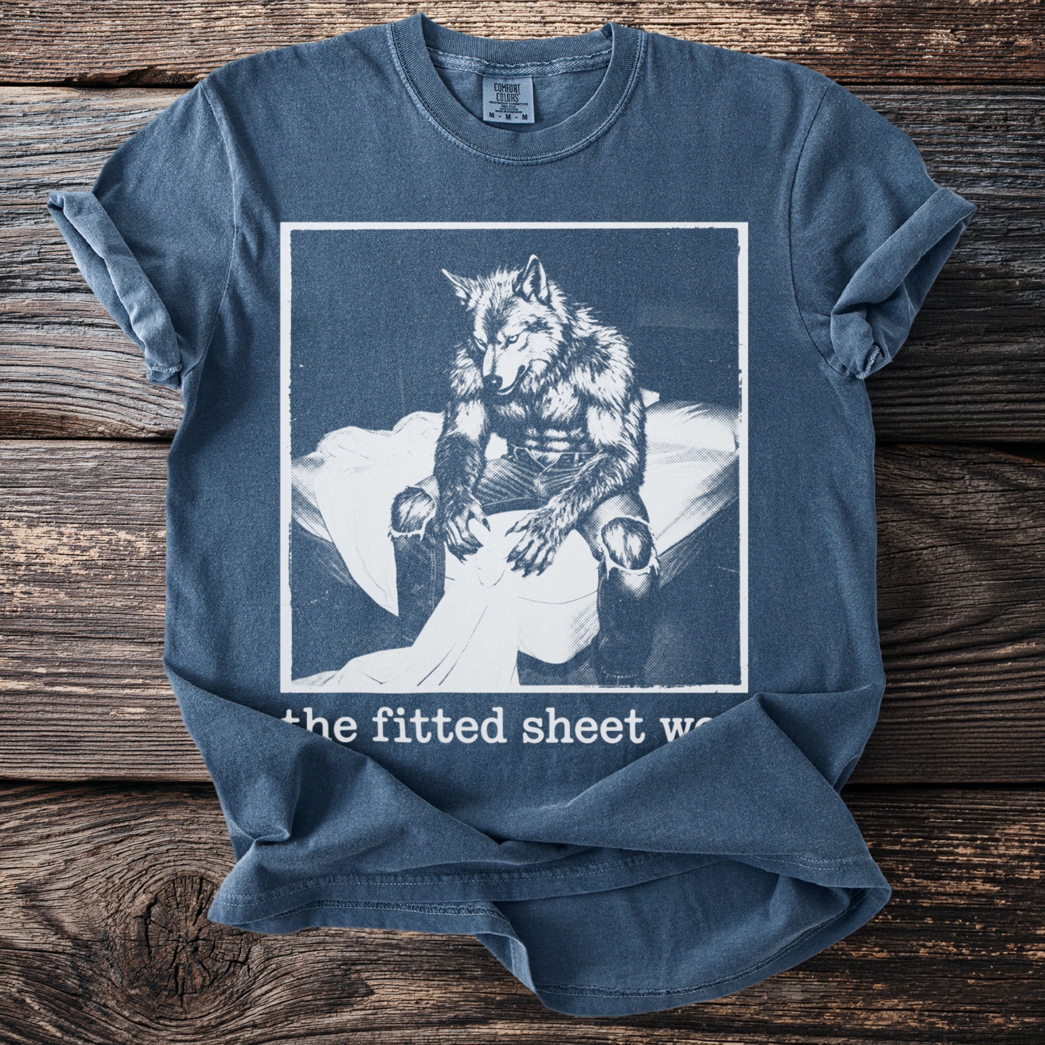 Werewolf sitting on a bed, printed on a blue t-shirt with text "the fitted sheet w".