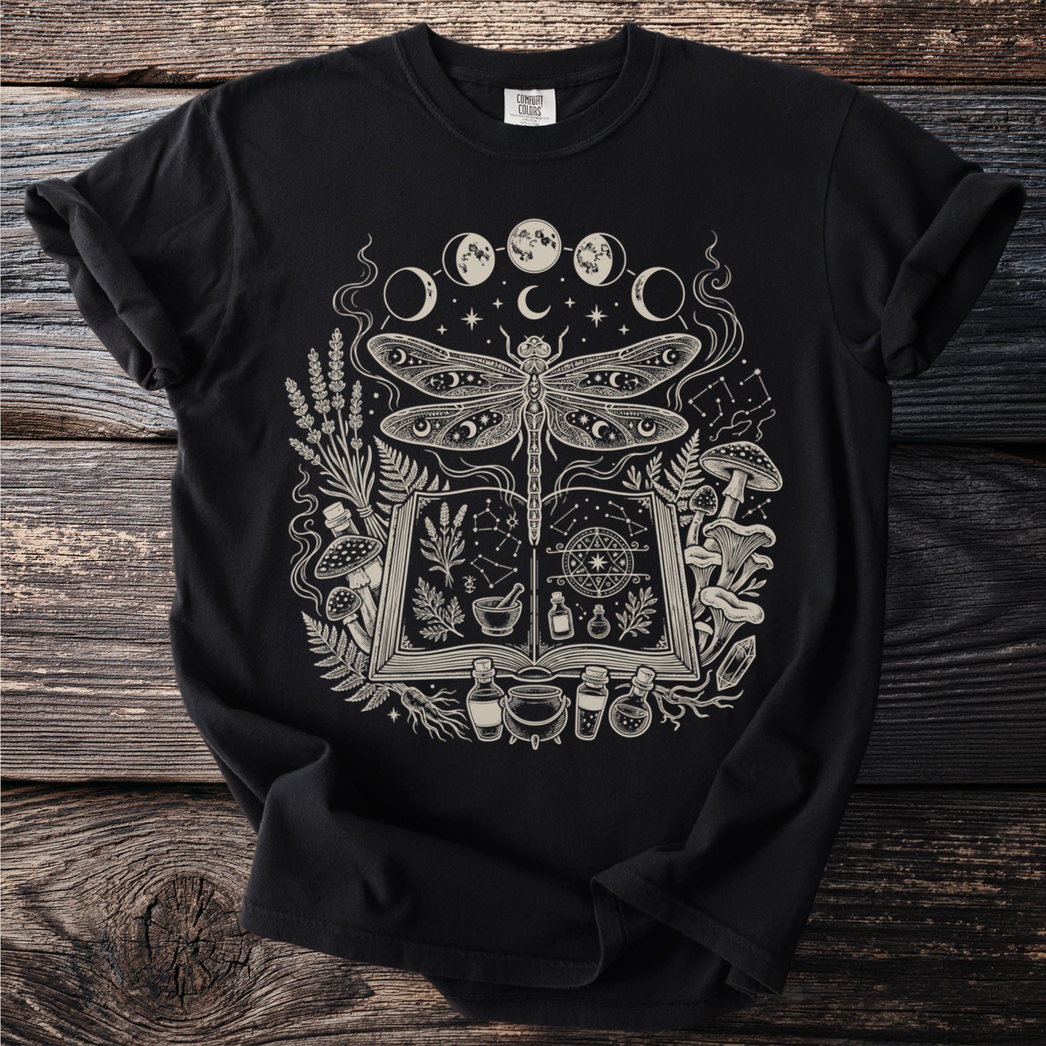 Black t-shirt with a mystical dragonfly, moon phases, potion bottles, and an open book design.