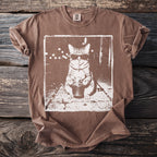 Brown t-shirt with a white graphic of a cat wearing sunglasses holding a drink.