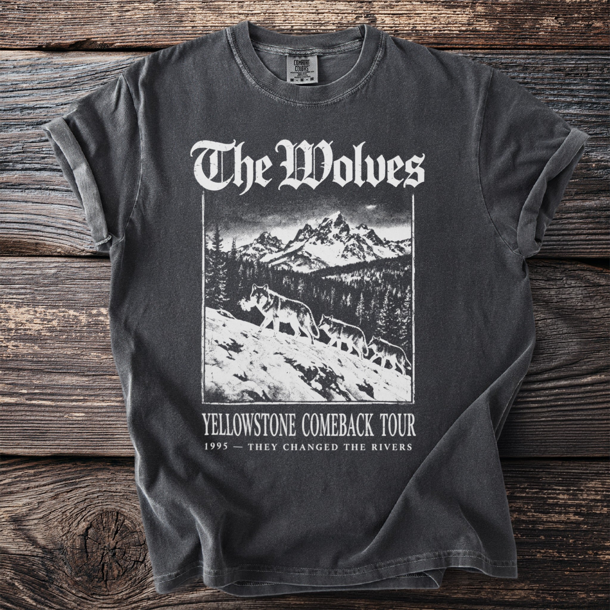 T-shirt with graphic of wolves walking across a snowy mountain landscape and text "The Wolves Yellowstone Comeback Tour".