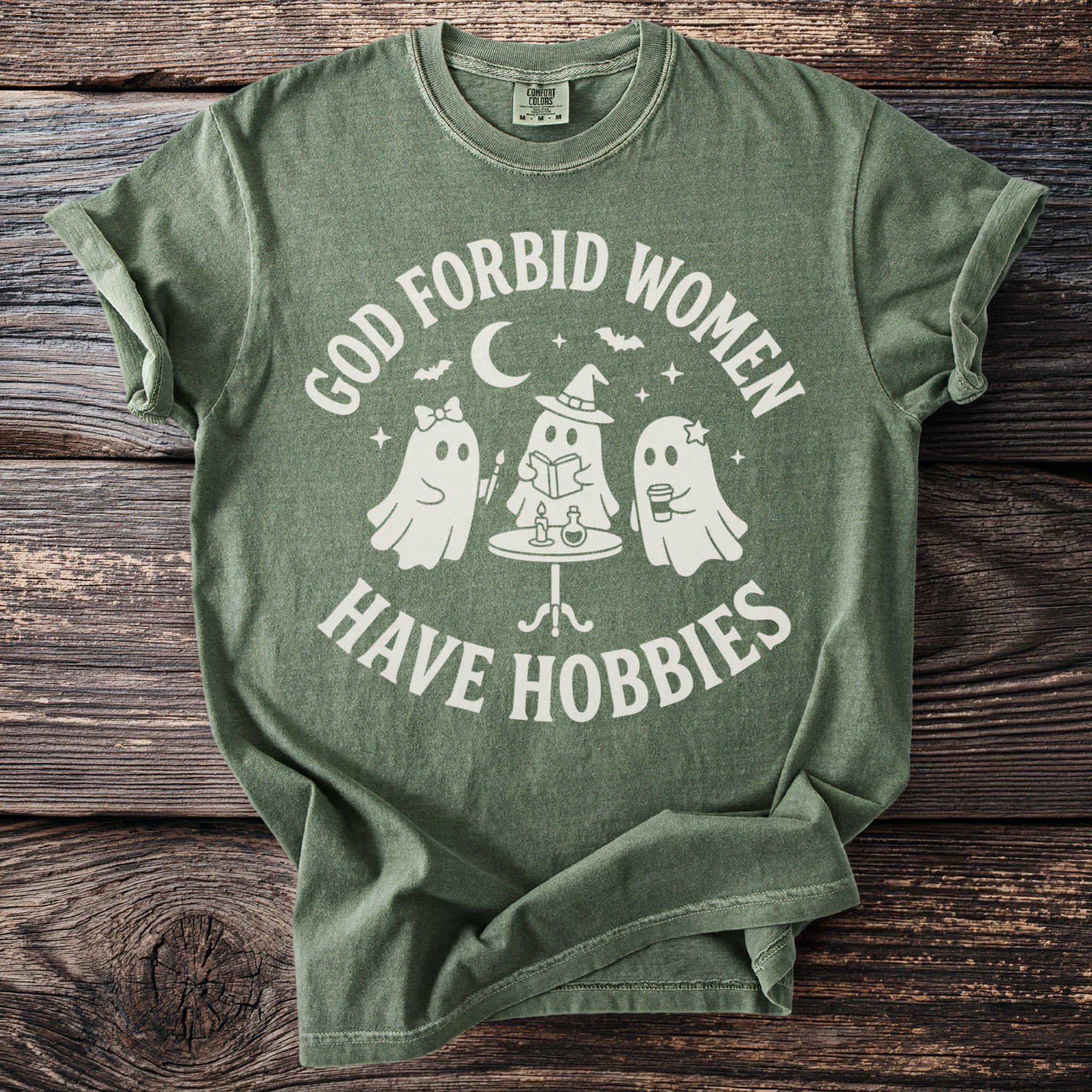 Green t-shirt with white text "God forbid women have hobbies" and three ghosts.