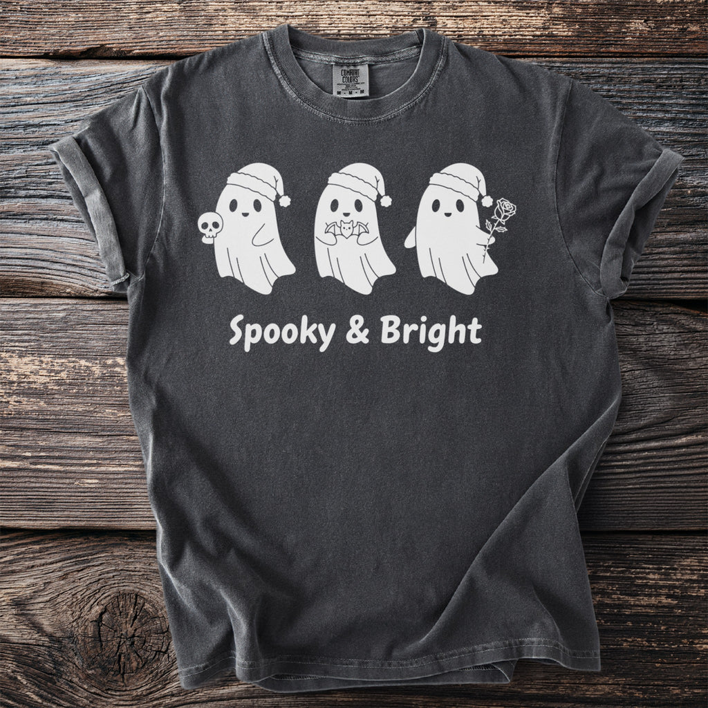 Three white ghosts in Santa hats, one holding a skull, on a dark gray t-shirt with "Spooky & Bright" text.