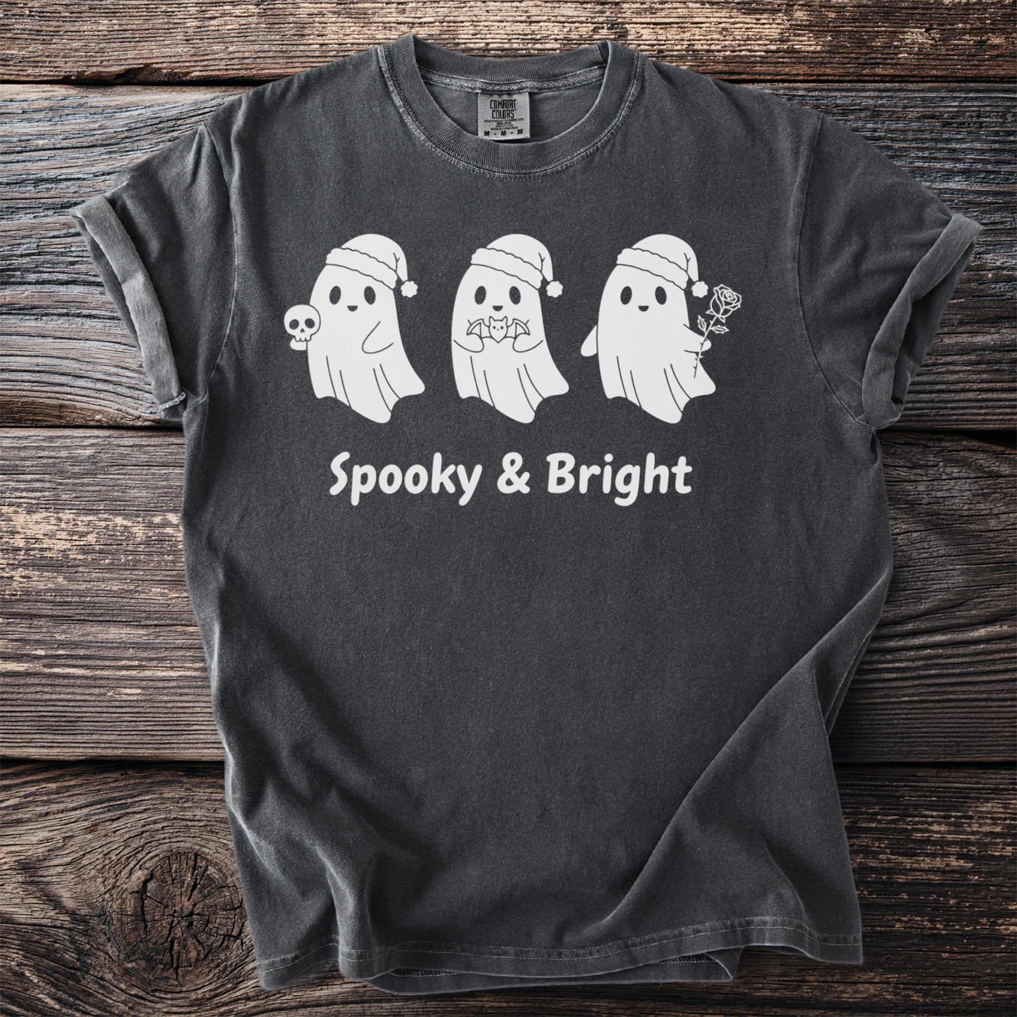 Three white ghosts in Santa hats, one holding a skull, on a dark gray t-shirt with "Spooky & Bright" text.