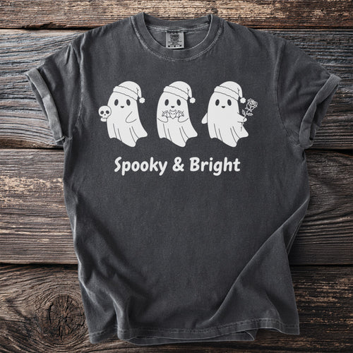 Three white ghosts in Santa hats, one holding a skull, on a dark gray t-shirt with "Spooky & Bright" text.