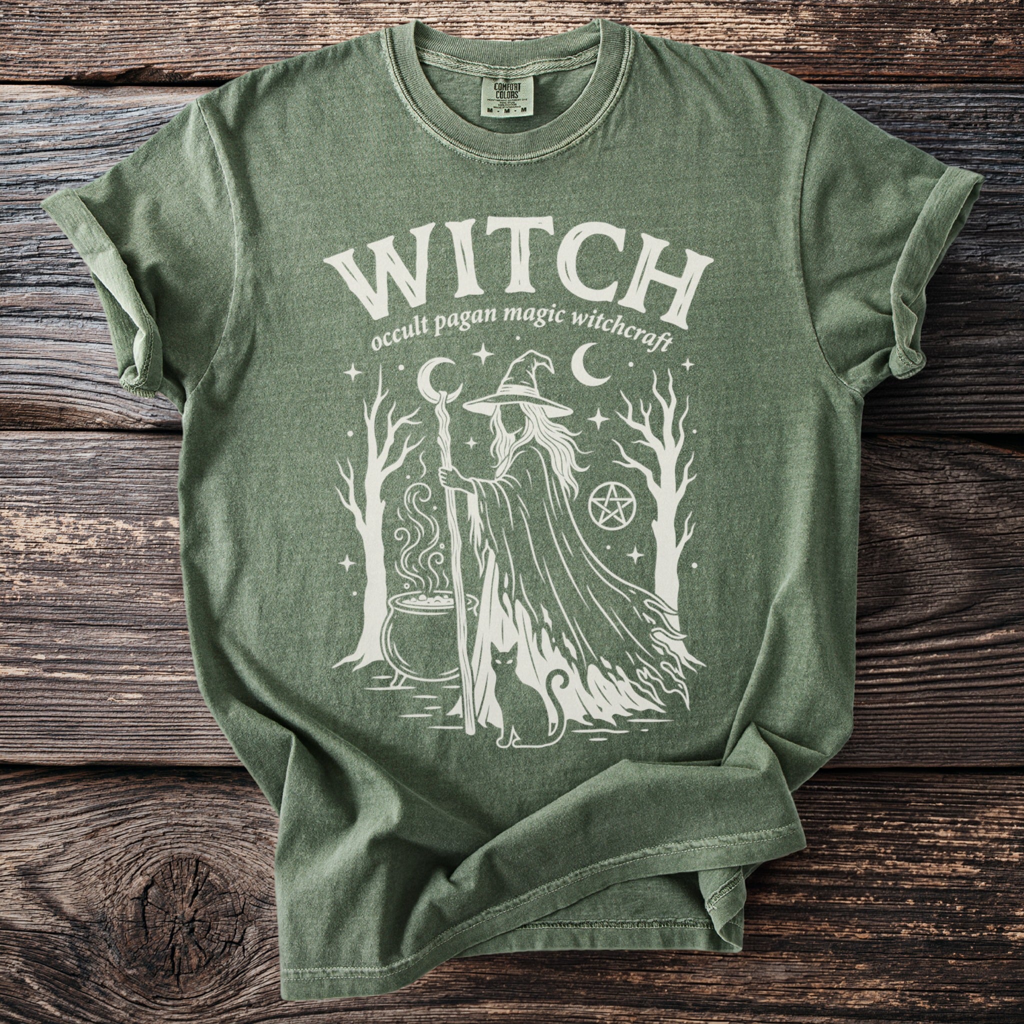 Green t-shirt with white graphic of a witch, cauldron, cat, trees, and stars.