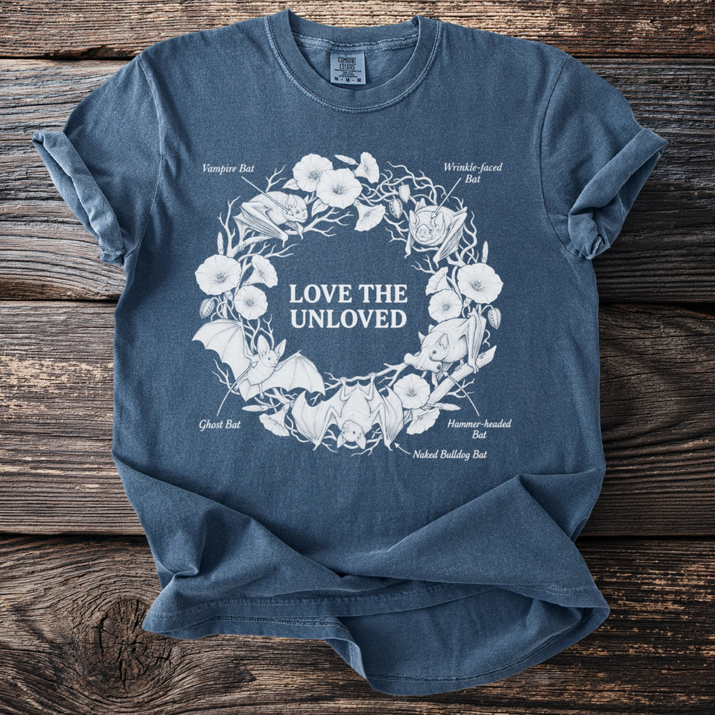 Blue t-shirt with white graphic of bats, flowers, and text "LOVE THE UNLOVED".