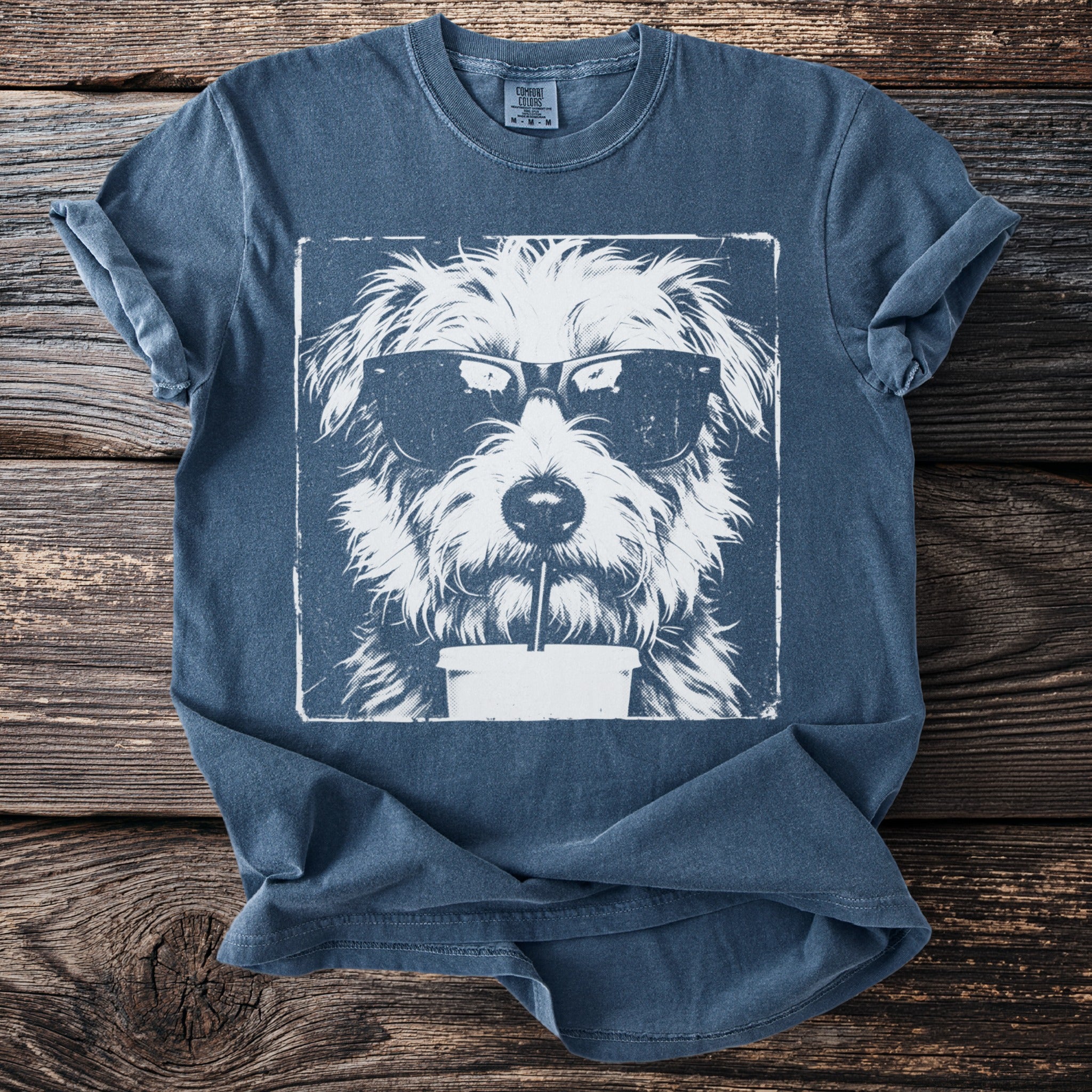 Blue t-shirt with graphic of white dog wearing sunglasses drinking from a straw.