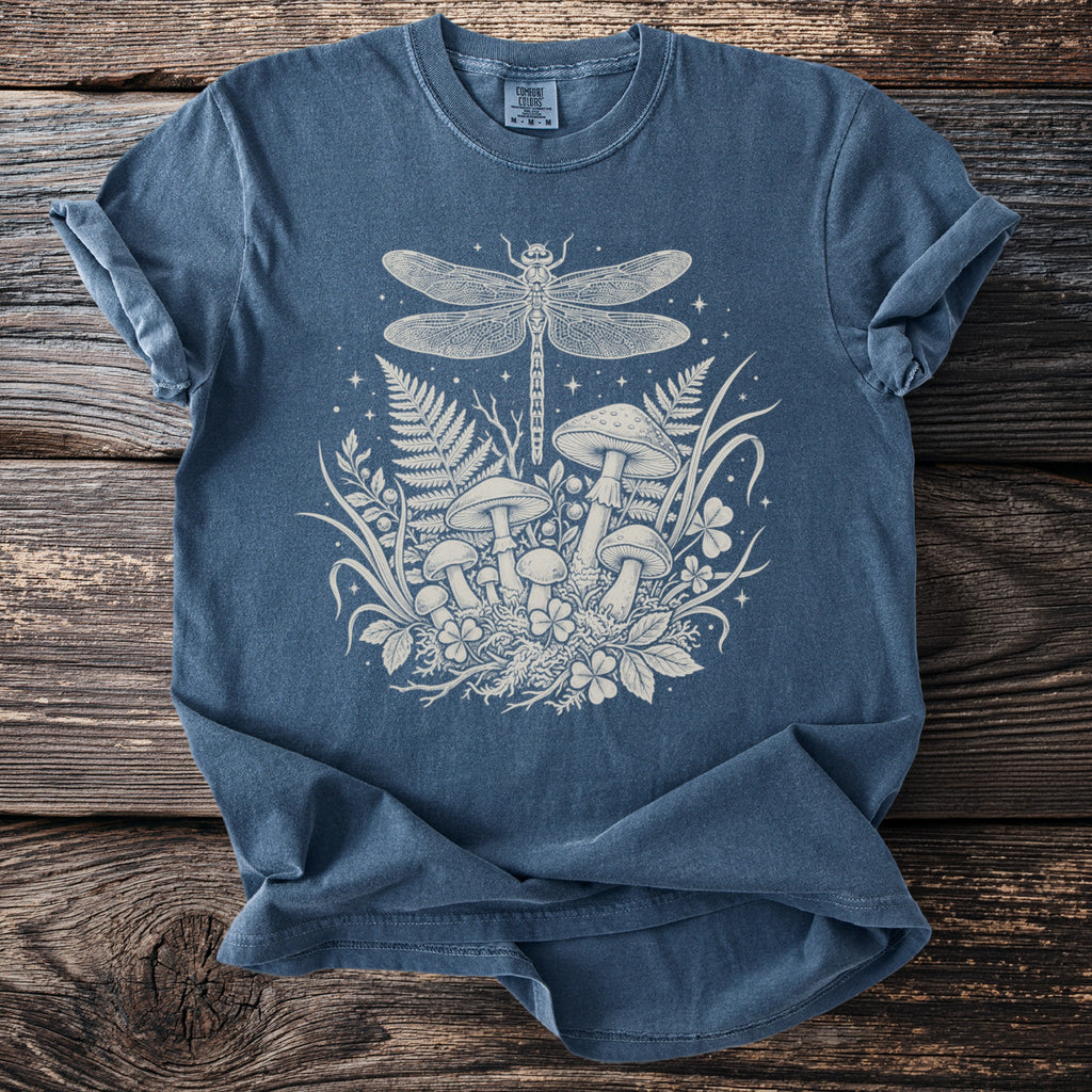 Blue t-shirt with white dragonfly and mushroom design on a wooden background.