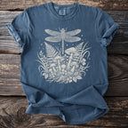 Blue t-shirt with white dragonfly and mushroom design on a wooden background.