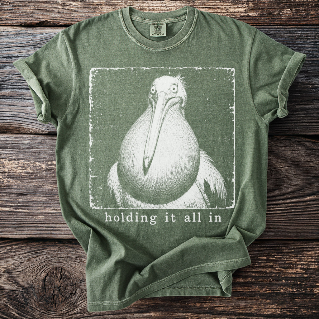 Green t-shirt with graphic of a pelican and text "holding it all in".