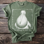 Green t-shirt with graphic of a pelican and text "holding it all in".