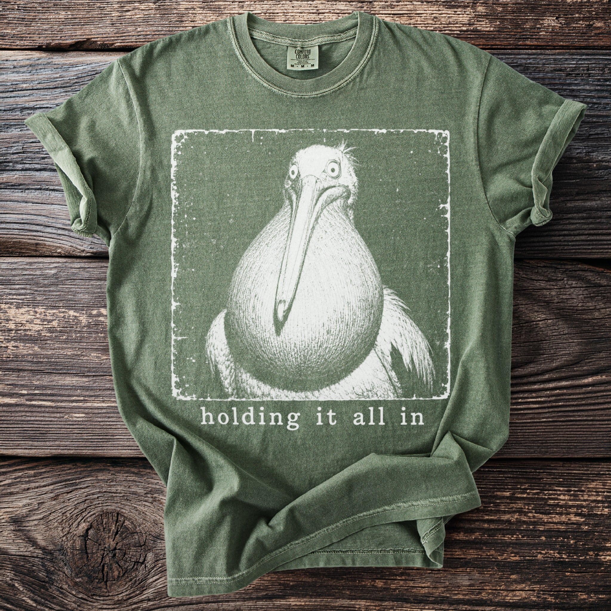 Green t-shirt with graphic of a pelican and text "holding it all in".