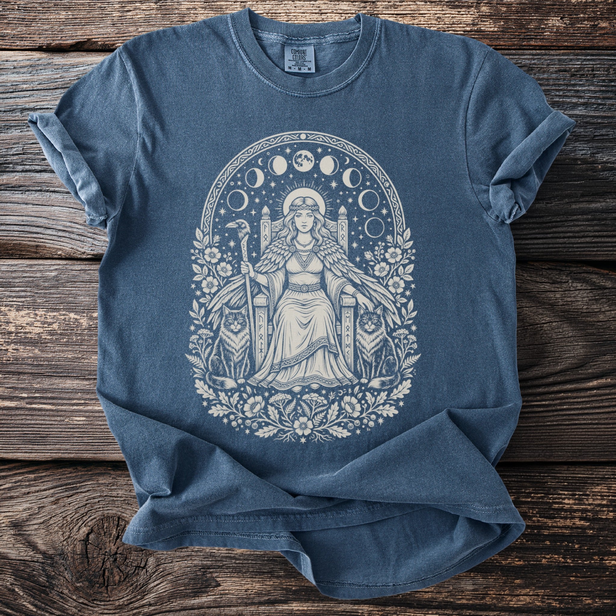 Blue t-shirt with a white graphic of a crowned woman on a throne between two cats.