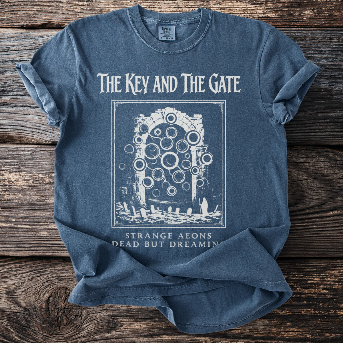Blue t-shirt with "The Key and The Gate" graphic and text "Strange Aeons Dead But Dreamin".