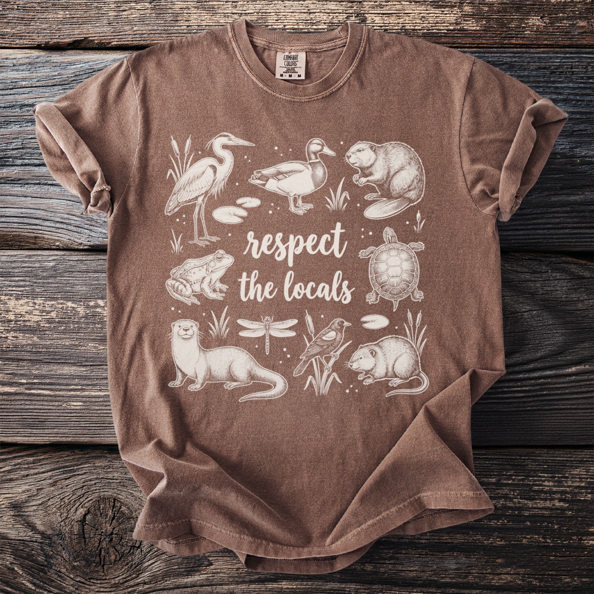 Brown t-shirt with cream illustration of wildlife and text "respect the locals".