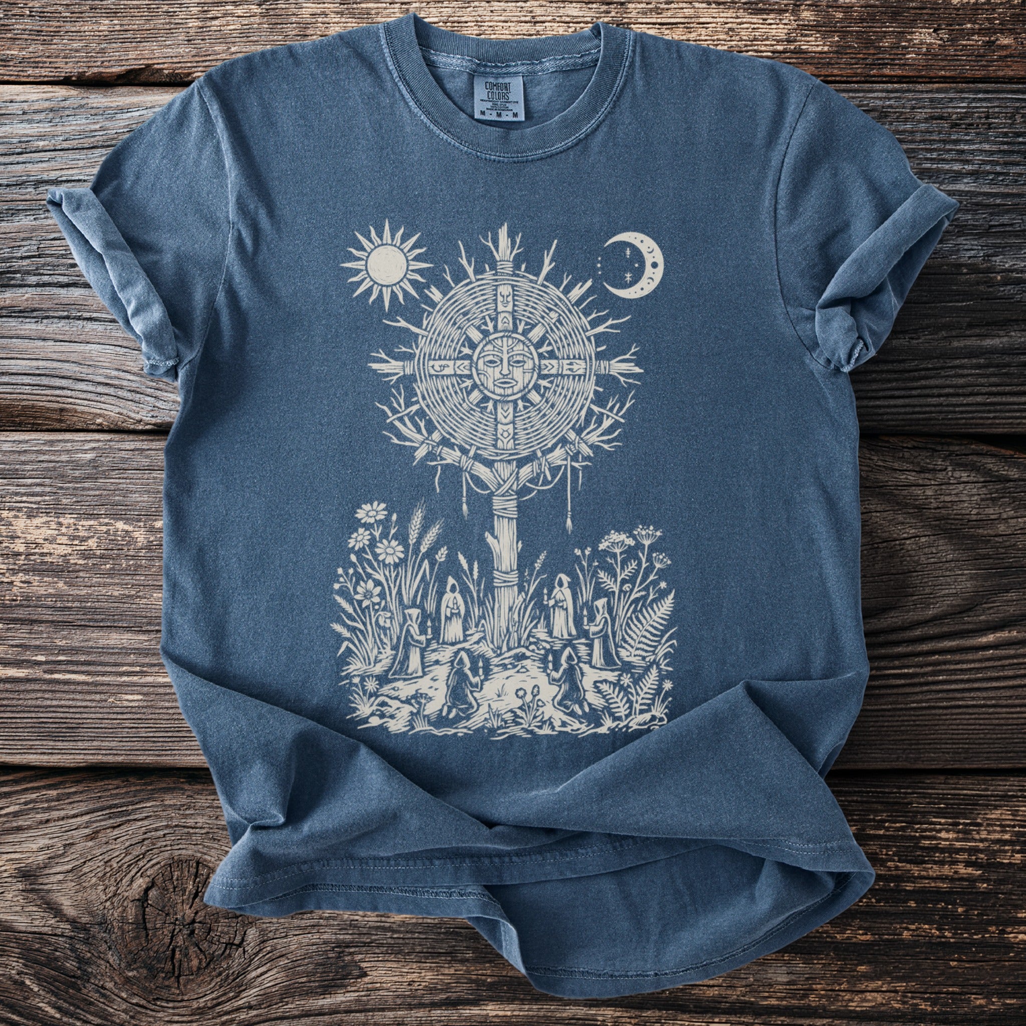 Blue t-shirt with sun, moon, and a gathering around a stylized tree.