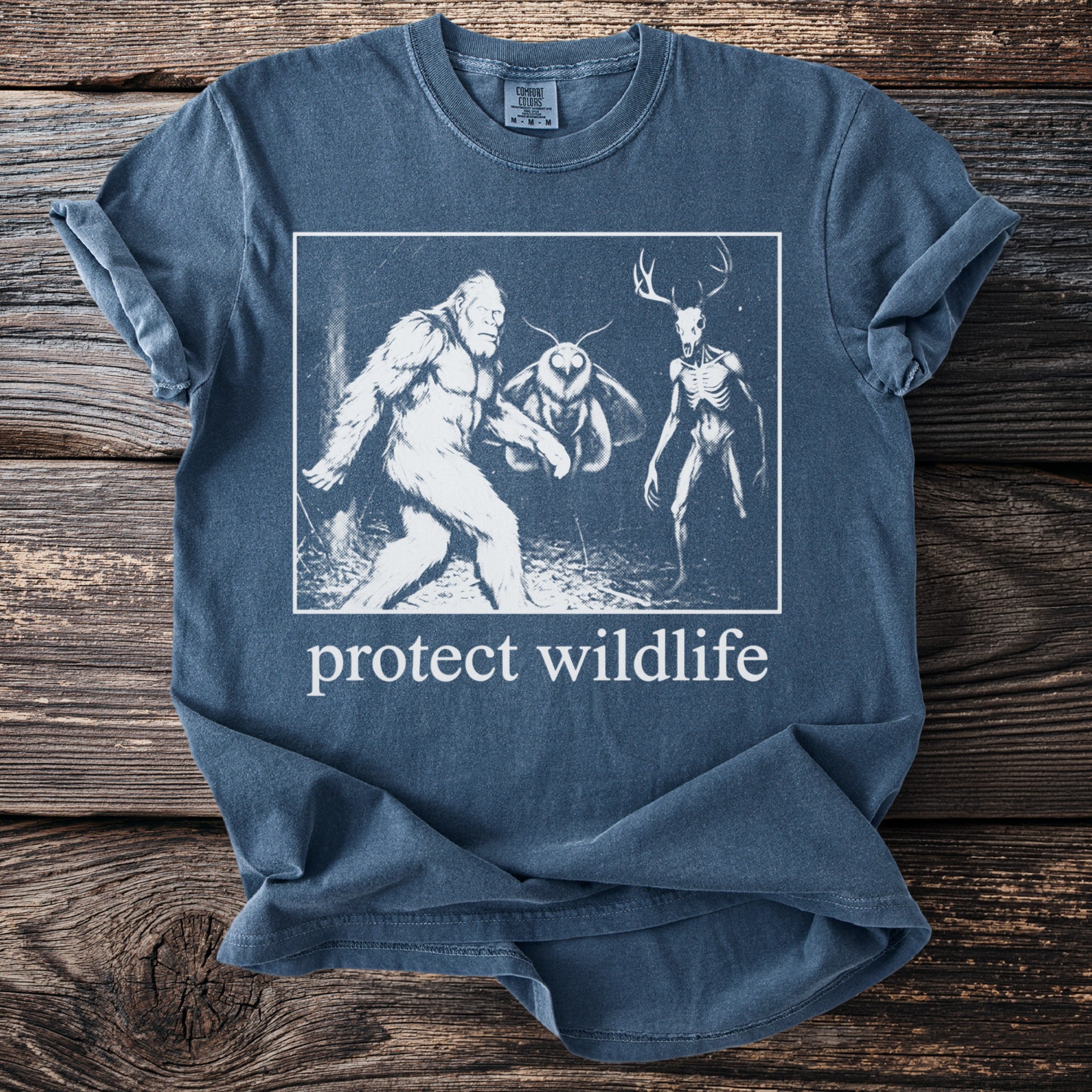 T-shirt graphic features Bigfoot, mothman, and skeleton deer with text "protect wildlife"