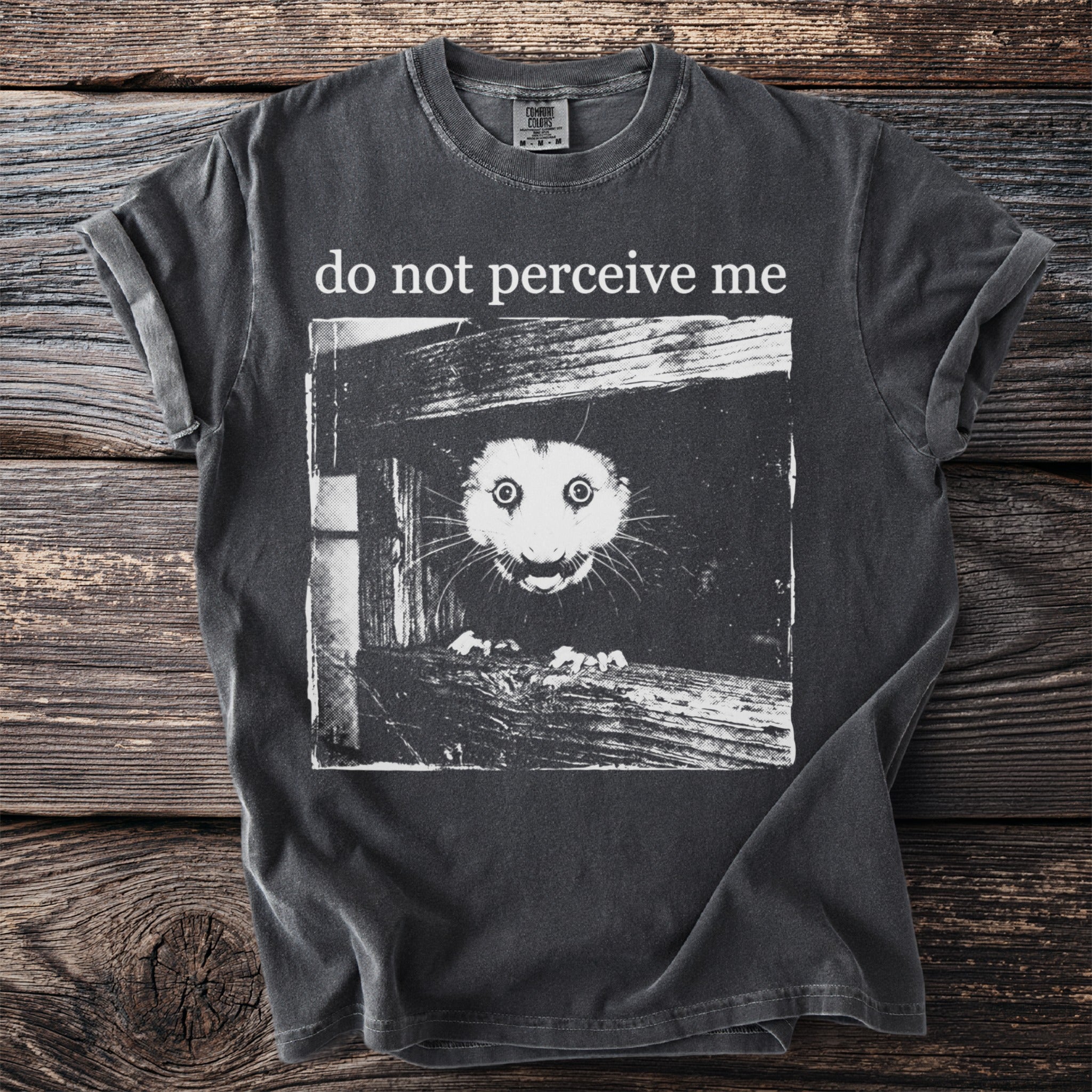 Dark gray T shirt with a bushbaby peering through wooden planks and “do not perceive me” text.