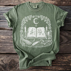 Green t-shirt with open book, moon, candles, sage, feather, and key graphic.