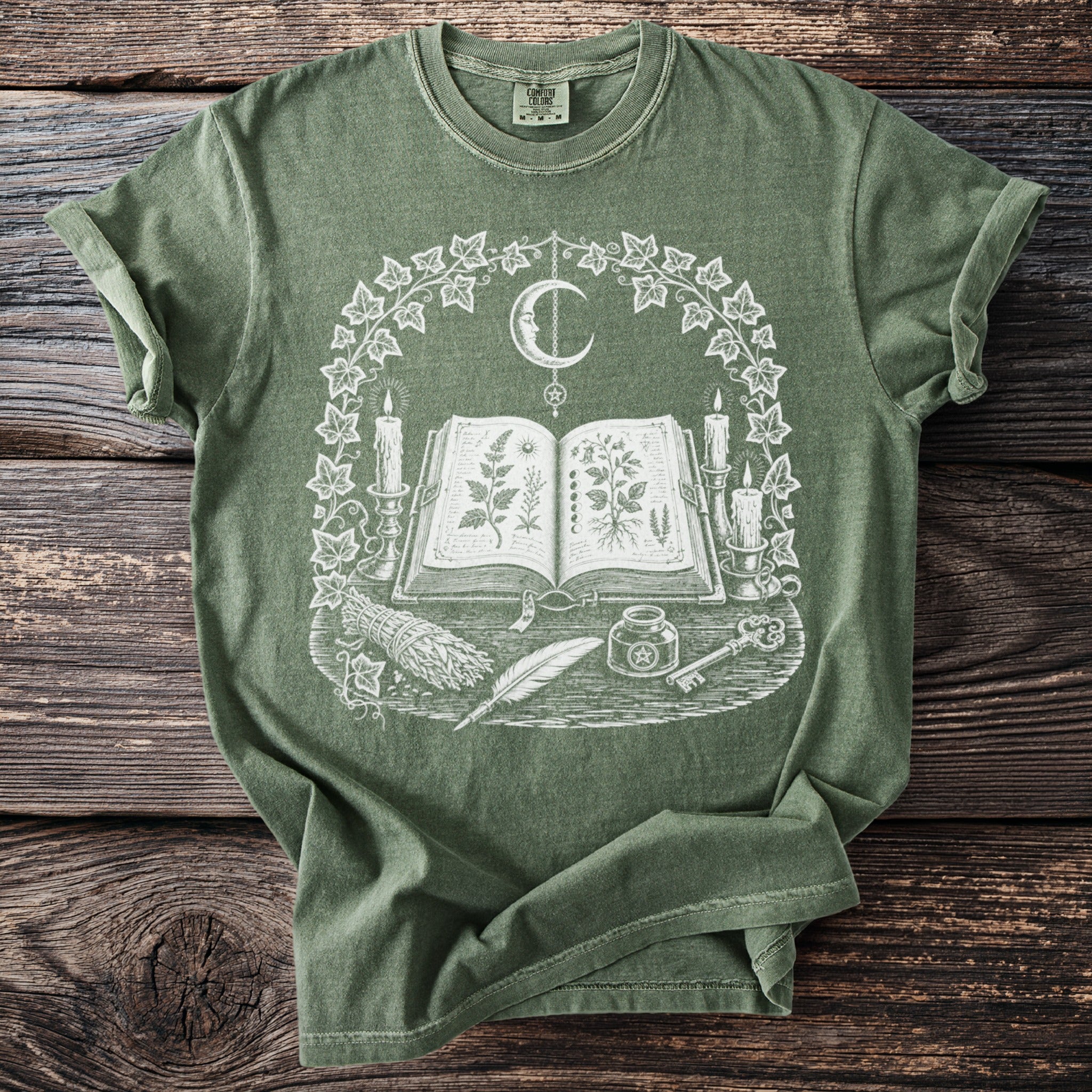 Green t-shirt with open book, moon, candles, sage, feather, and key graphic.