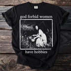 Black t-shirt with text "god forbid women have hobbies" and a vintage illustration.