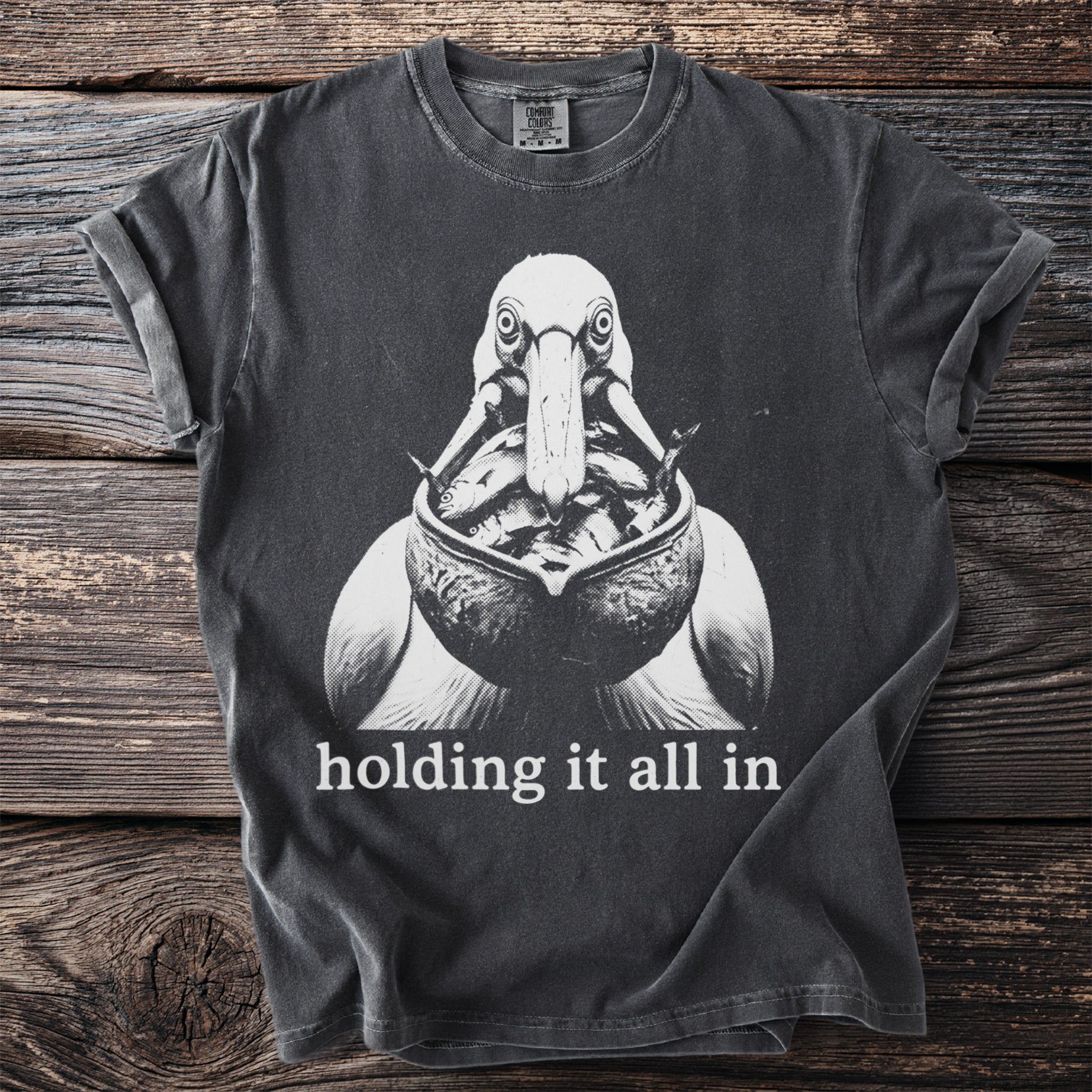 T-shirt with black and white graphic of a pelican with fish, and text "holding it all in."