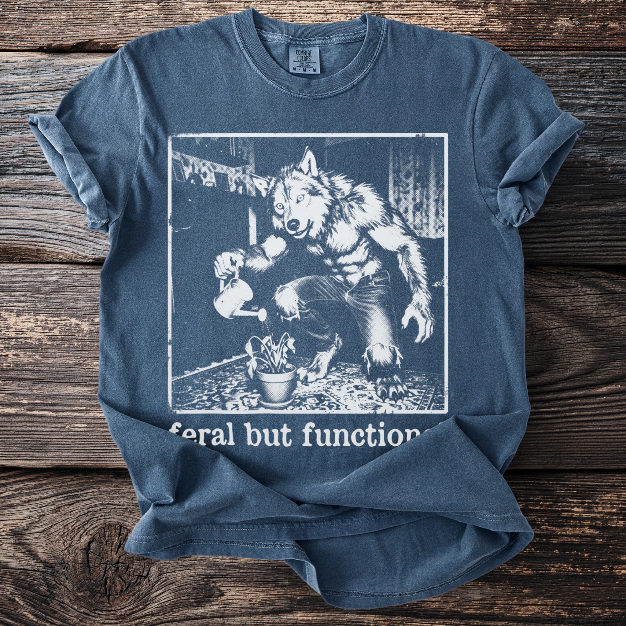 Werewolf watering a plant with text "feral but function" on a blue t-shirt.