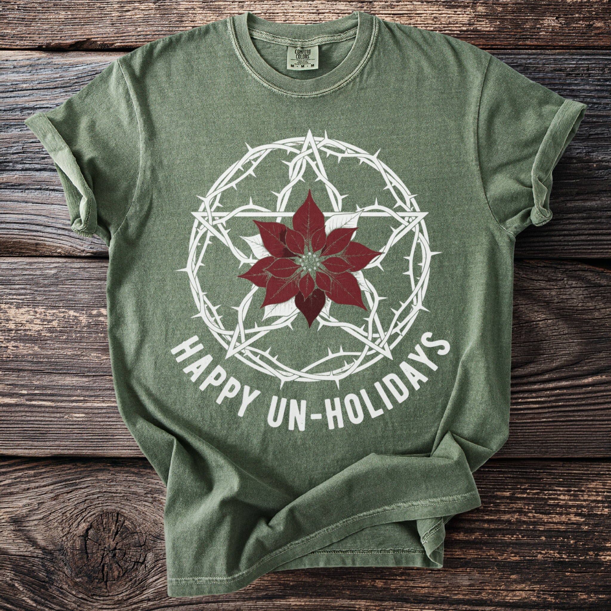 Green t-shirt with white thorny star, poinsettia, and text: Happy Un-Holidays.