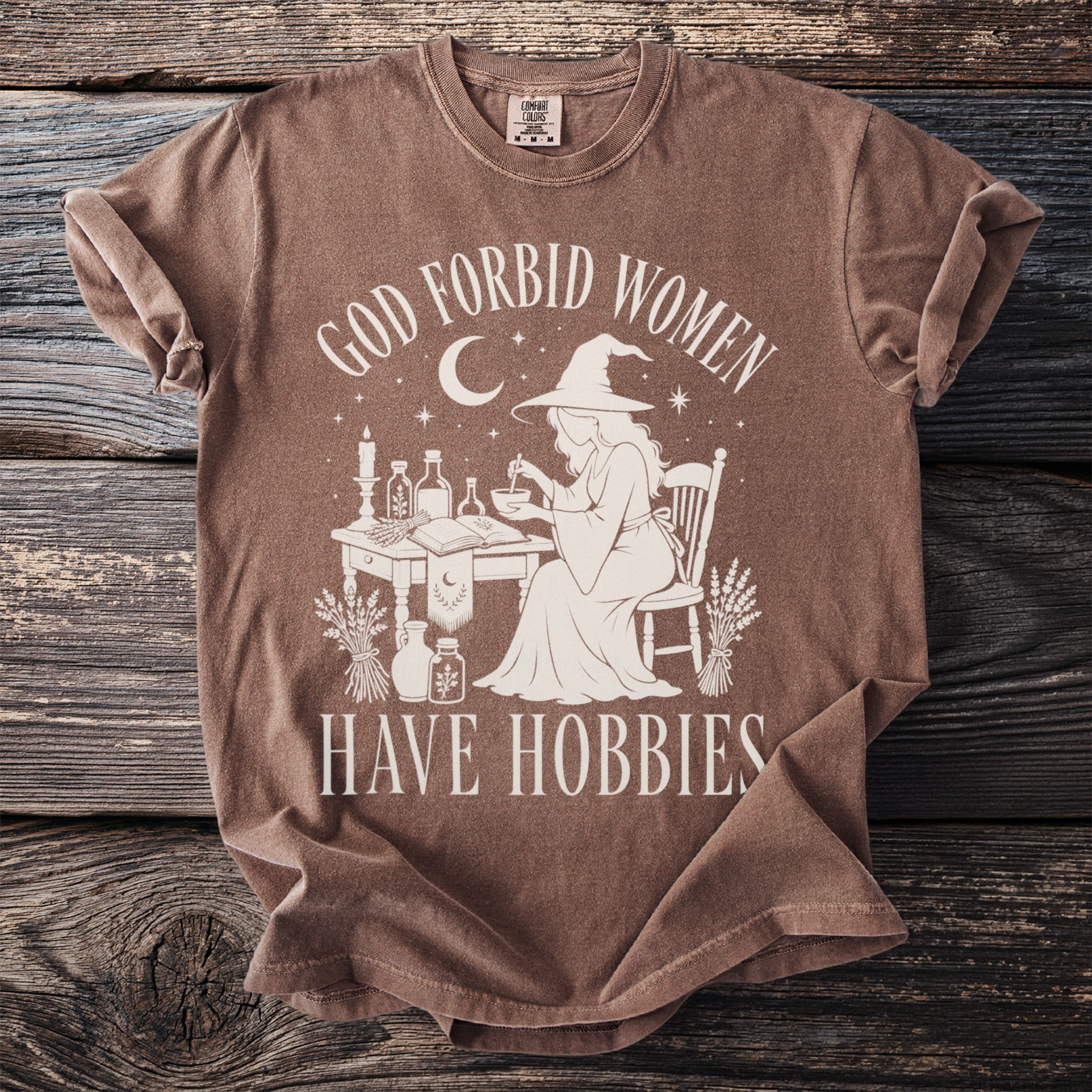 Brown t-shirt with graphic of witch and text "God forbid women have hobbies."