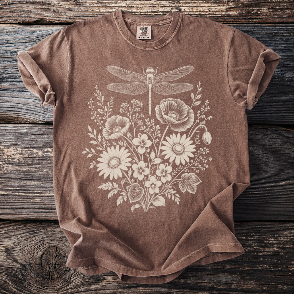 Brown t-shirt with a white dragonfly and floral print on a wooden background.