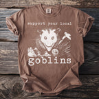 Brown t-shirt with opossum graphic and text "support your local goblins".