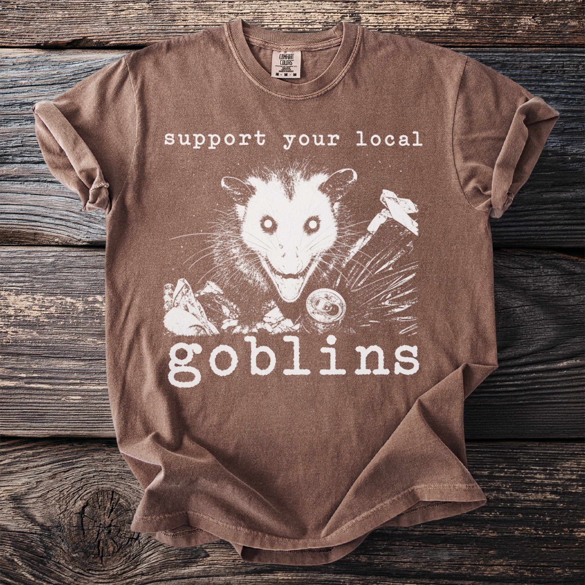 Brown t-shirt with opossum graphic and text "support your local goblins".