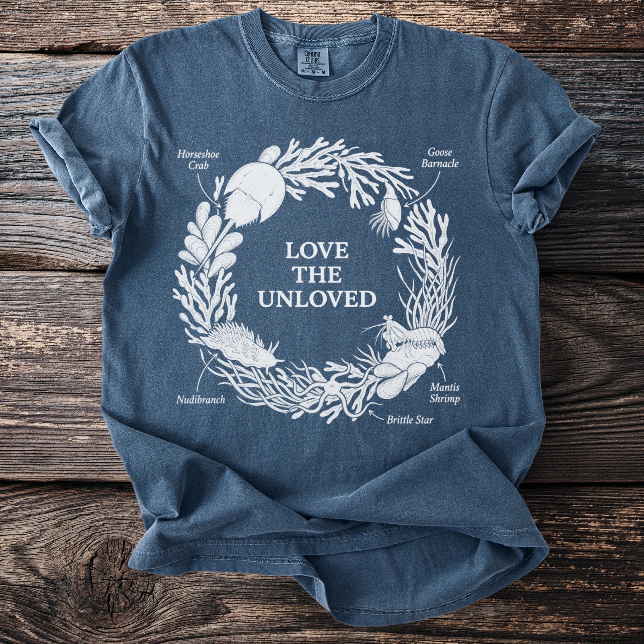 Blue t-shirt with white graphic of sea creatures forming a circle with text "LOVE THE UNLOVED".