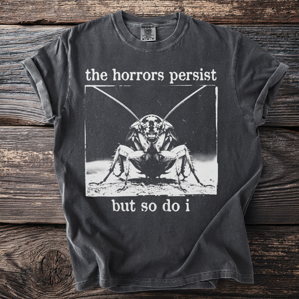 Dark gray t-shirt with a black and white graphic of a cockroach and text: "the horrors persist but so do i"