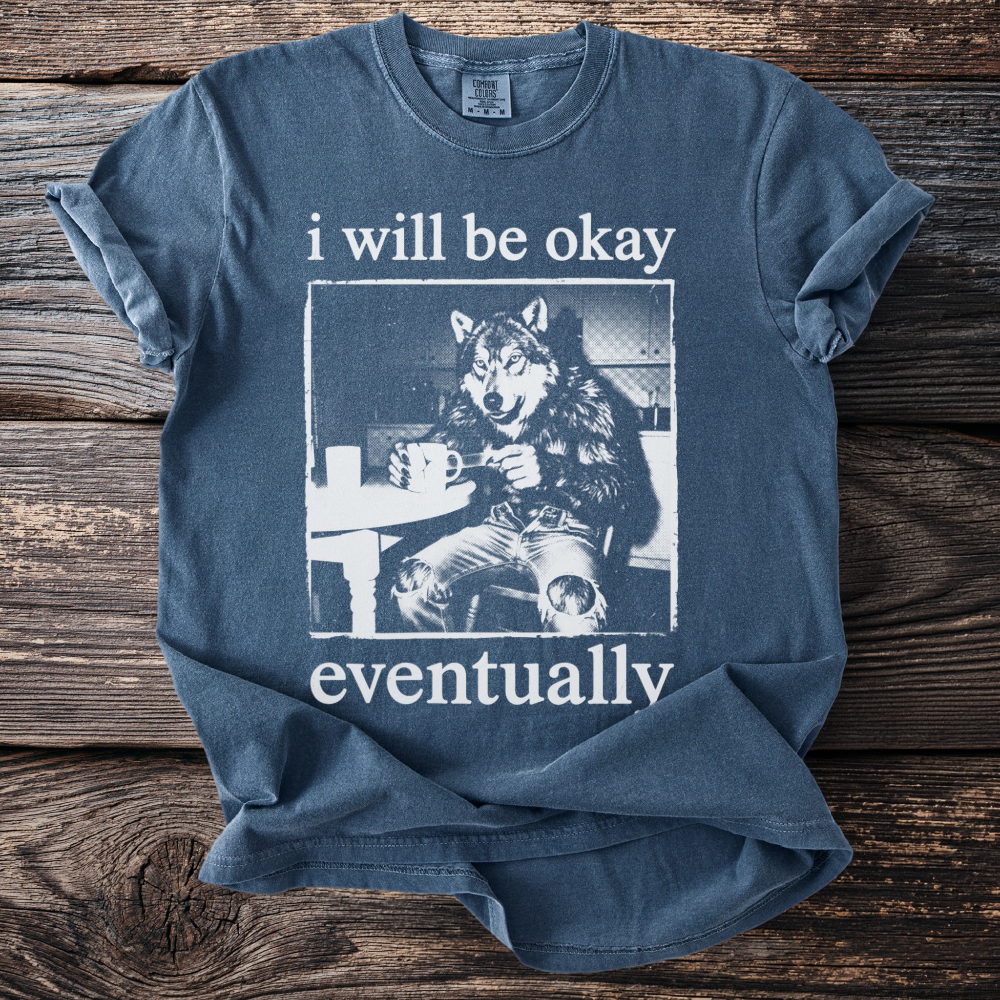 Blue t-shirt with a graphic of a wolf wearing jeans and holding a mug, with text.