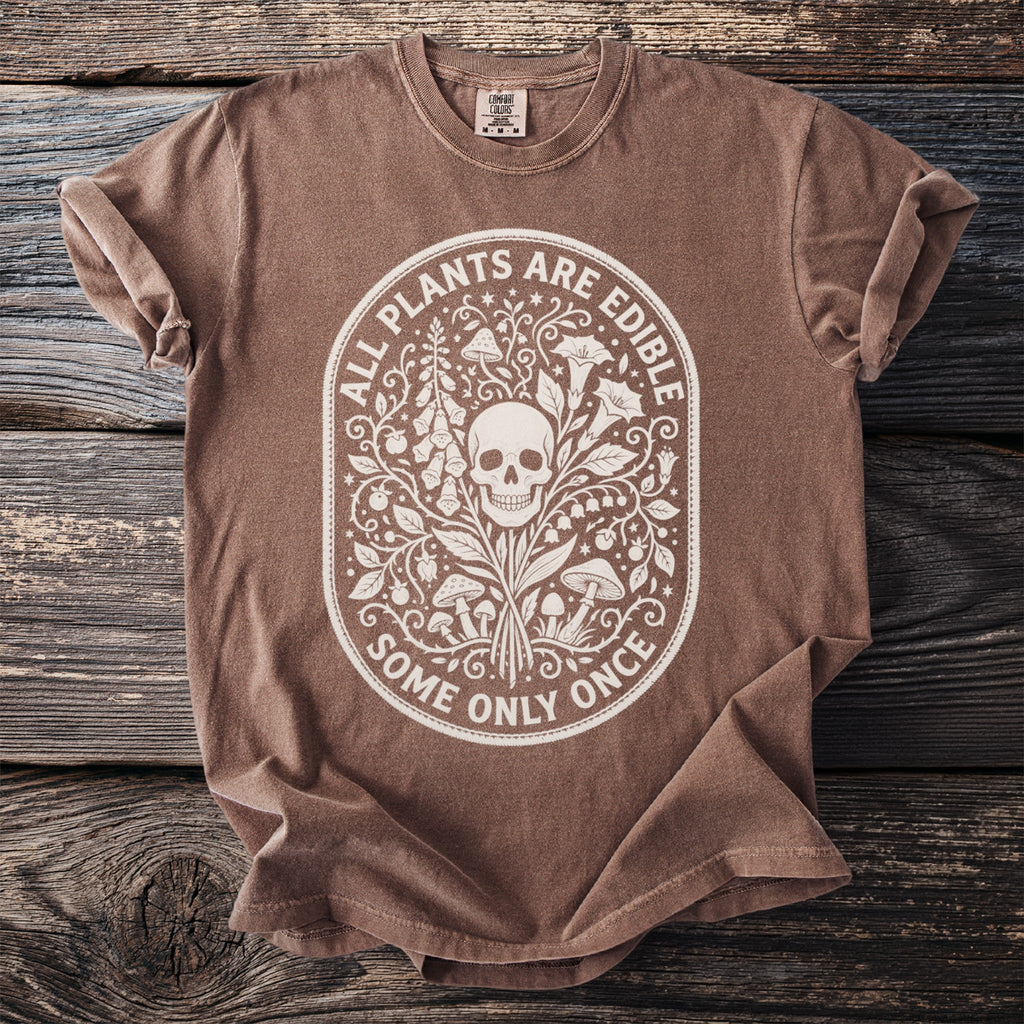 Brown t-shirt with white ornamental design of skull, plants, and mushrooms with text.