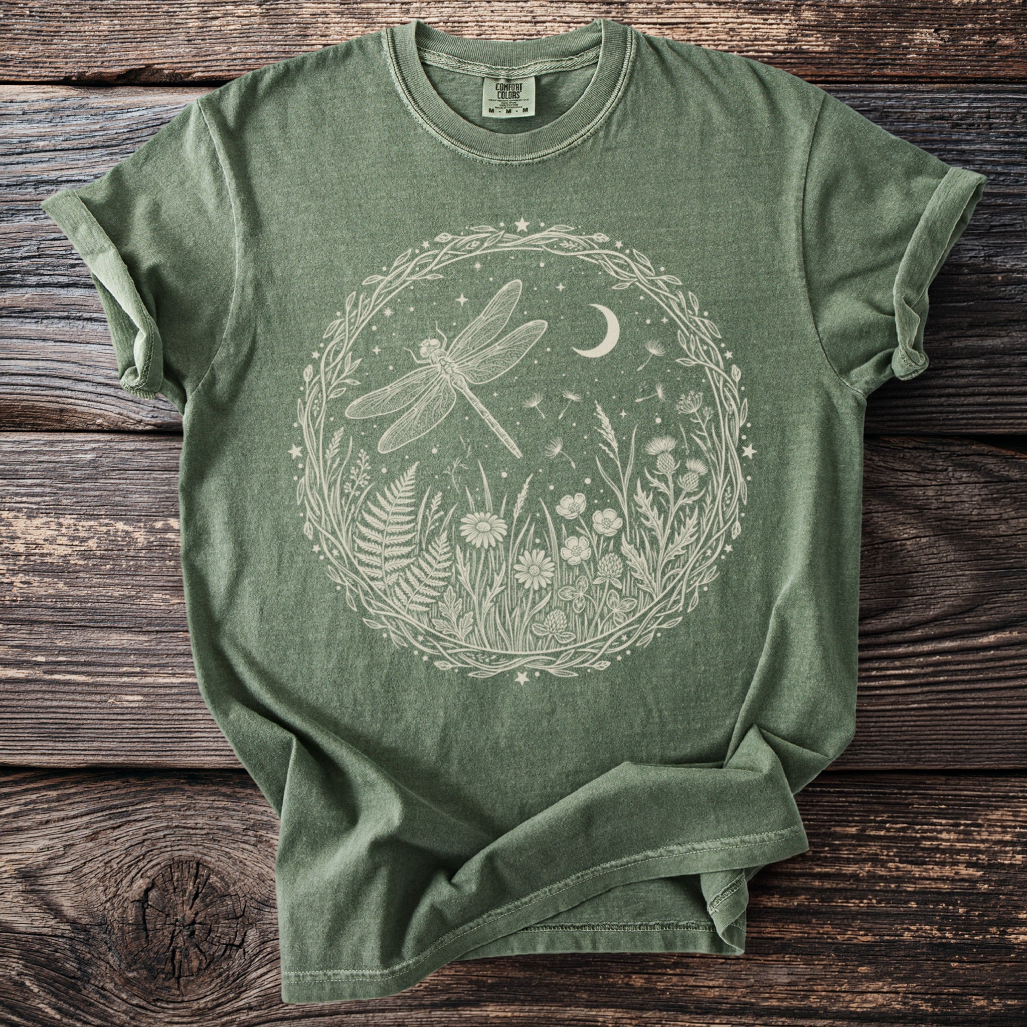 Olive green t-shirt with a cream line art circle of a dragonfly in a meadow.