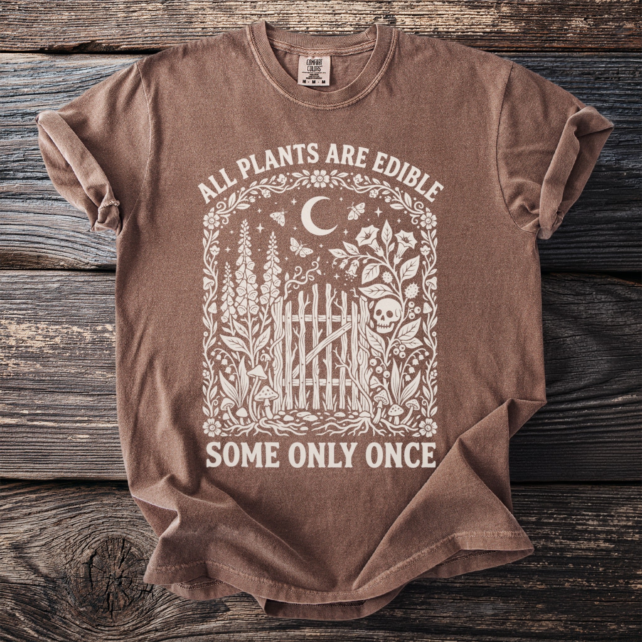 Brown Comfort Colors t-shirt with "ALL PLANTS ARE EDIBLE SOME ONLY ONCE" text and floral skull design.
