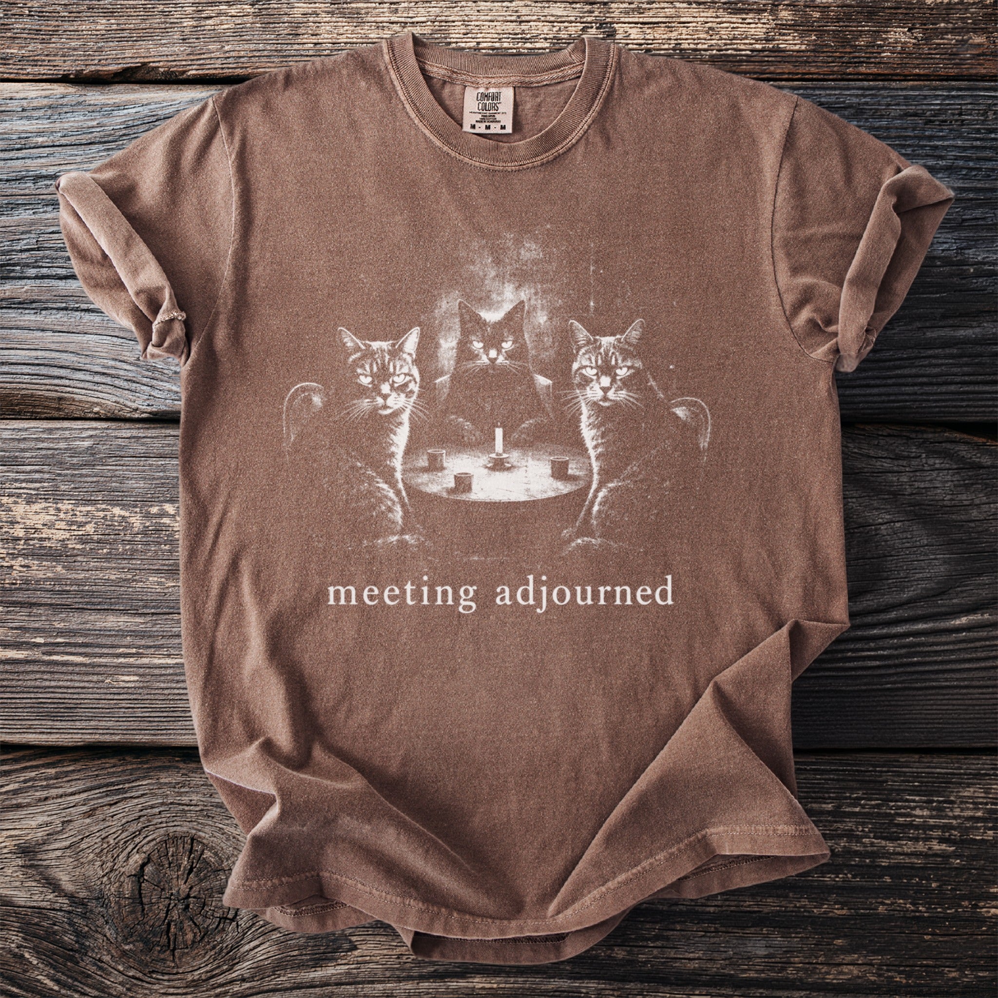 Brown t-shirt with three cats sitting around a table with a candle, text "meeting adjourned".