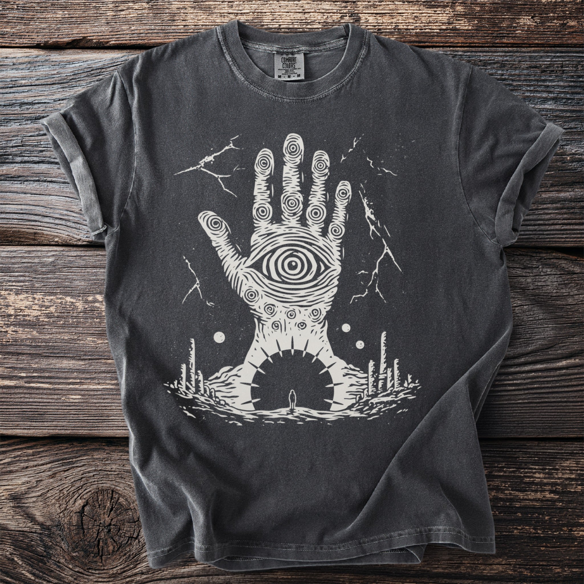 Dark gray t-shirt with white graphic of a hand with an eye and surreal landscape.
