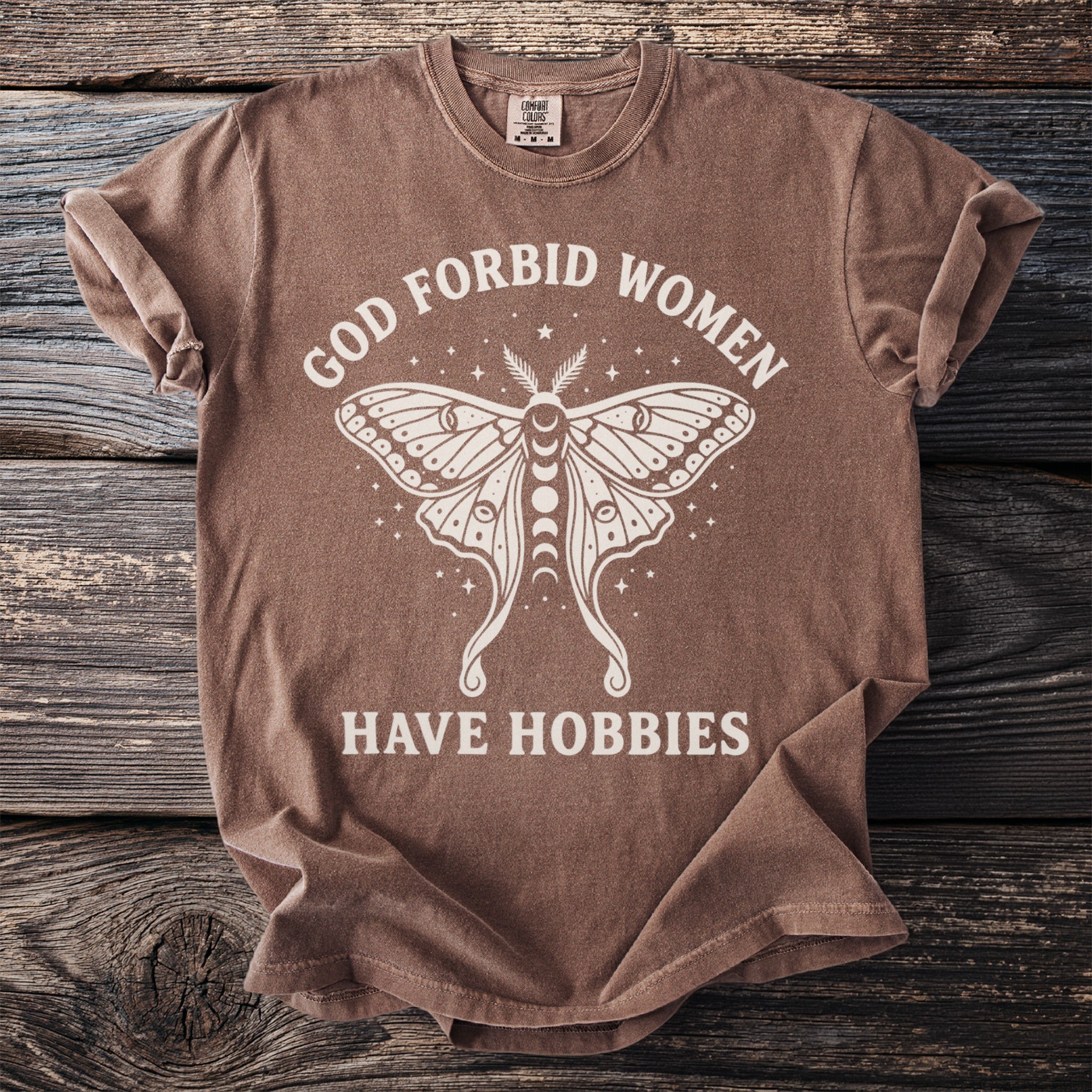 Brown t-shirt with a white moth graphic and text "GOD FORBID WOMEN HAVE HOBBIES".