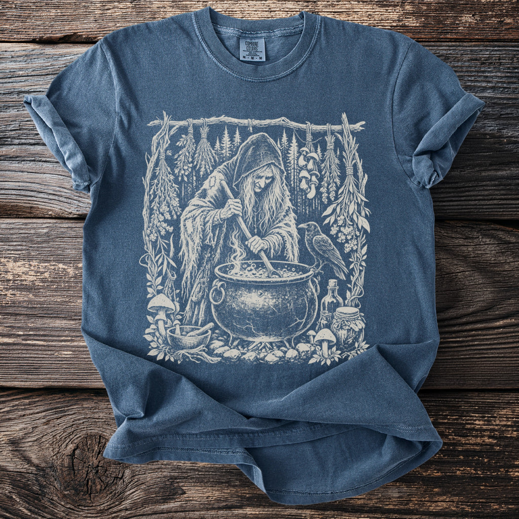 Witch stirring a cauldron with herbs, raven, and potion bottles illustration on t-shirt.