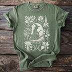Green t-shirt with a white graphic of a witch surrounded by plants and roots.