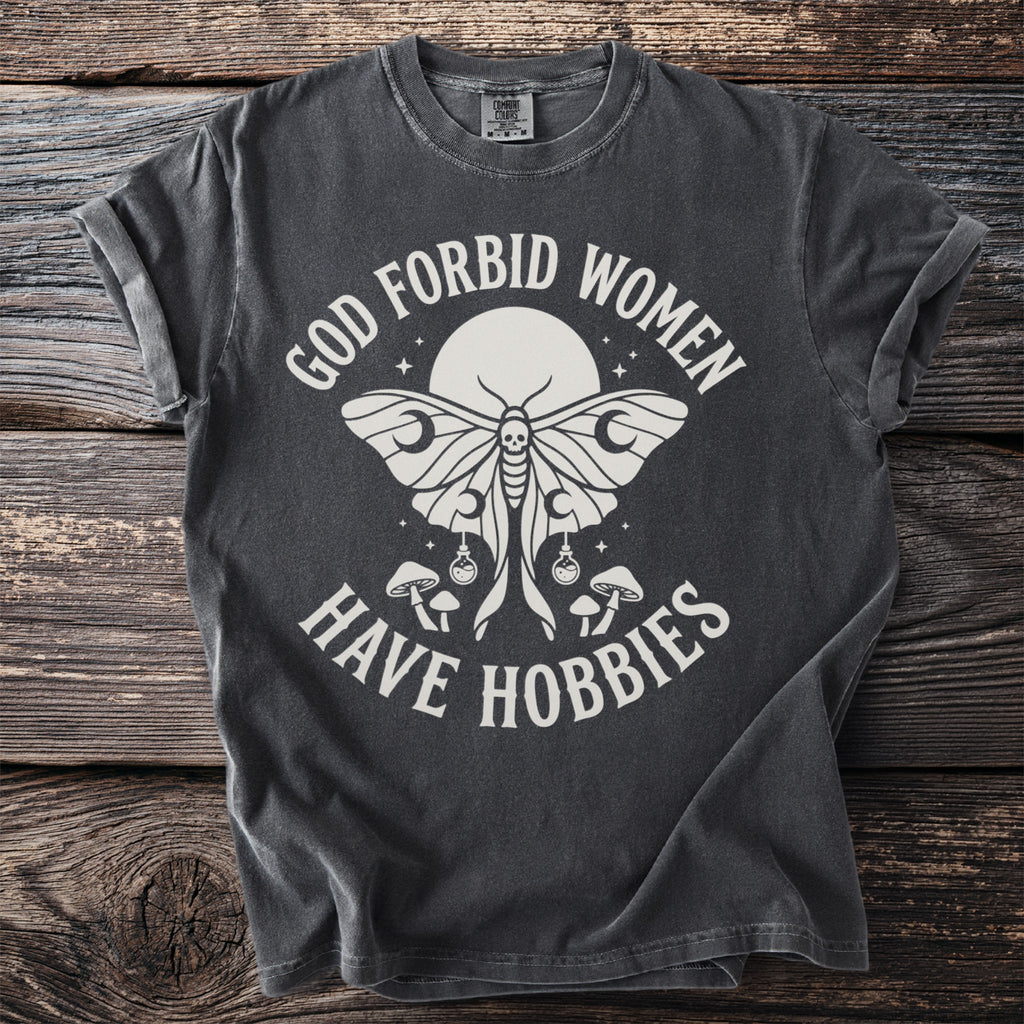 Dark grey t-shirt with white text and moth graphic reading "God forbid women have hobbies."