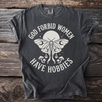 Dark grey t-shirt with white text and moth graphic reading "God forbid women have hobbies."