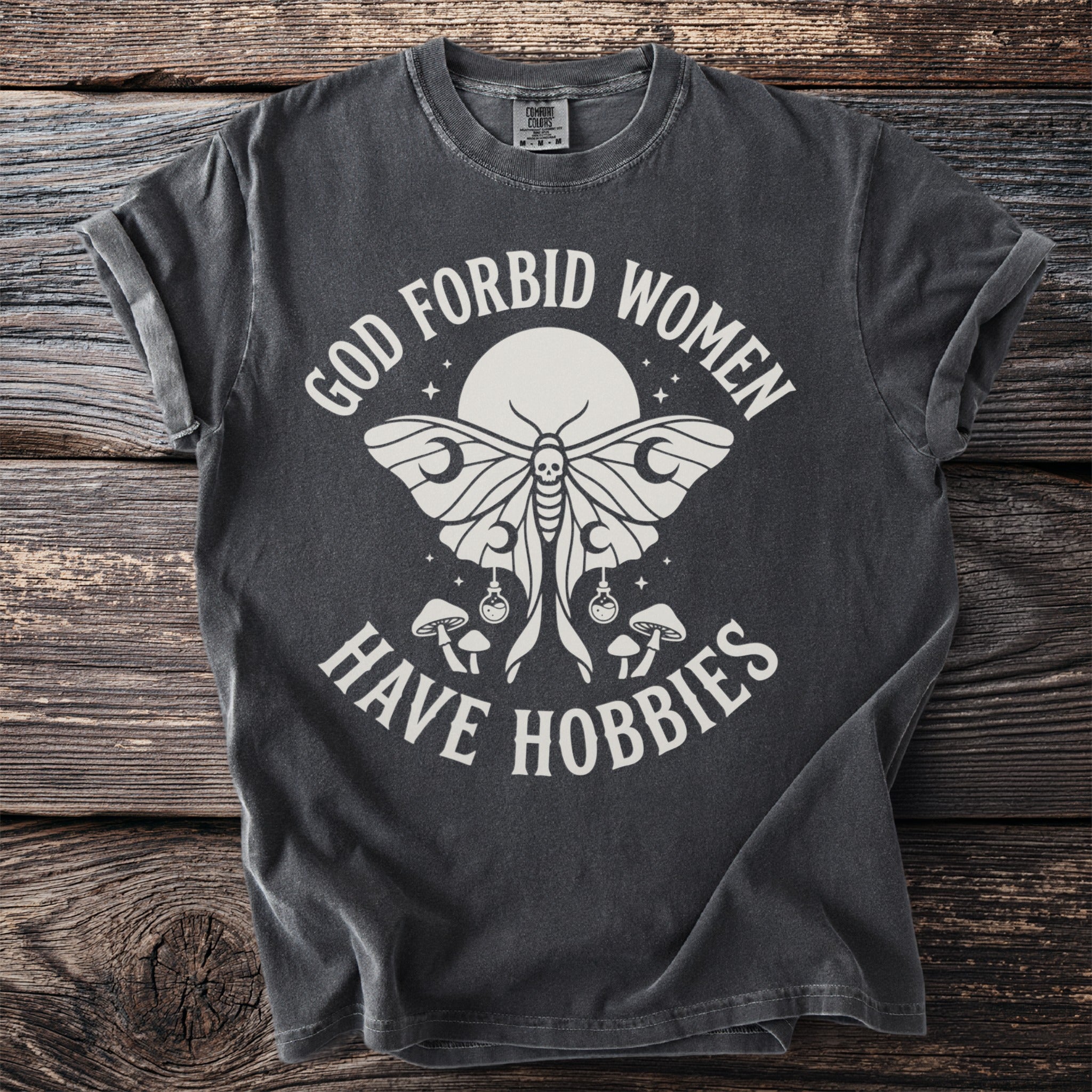 Dark grey t-shirt with white text and moth graphic reading "God forbid women have hobbies."