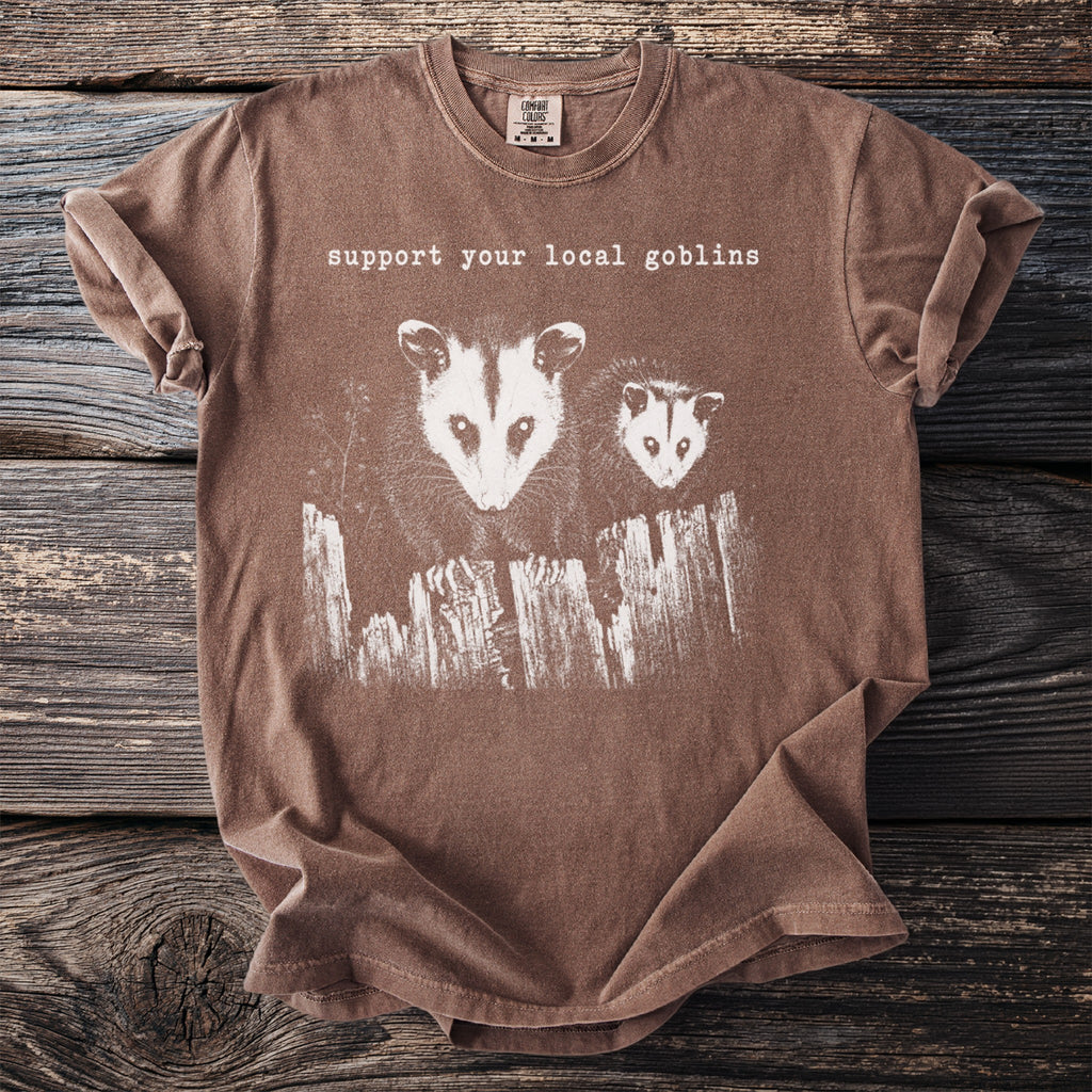 Brown t-shirt with "support your local goblins" text and two opossums over a fence.